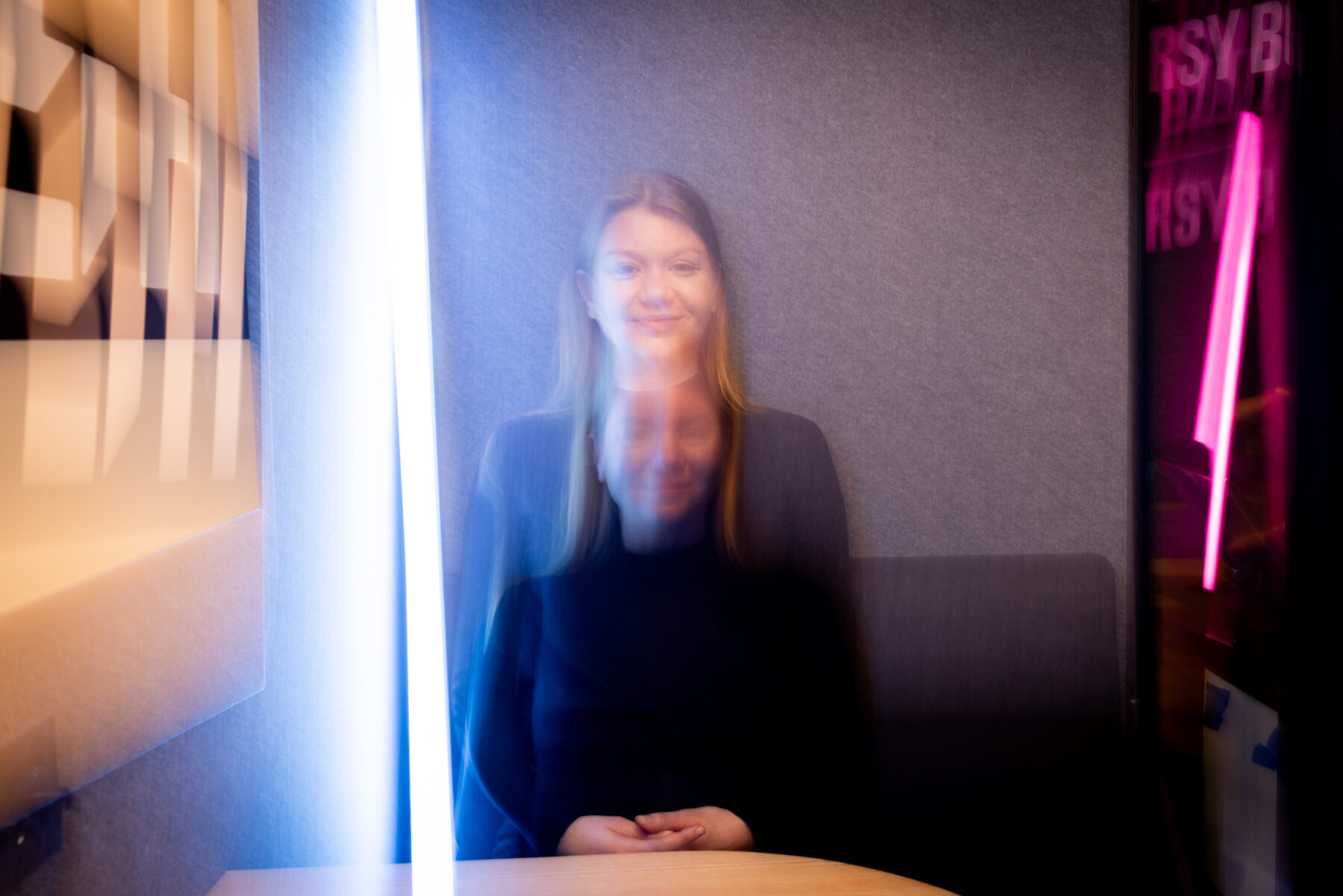 تجلس إيريكا سافولينين في كشك صغير مضاء بأضواء ساطعة تخلق تأثيرًا ضبابيًا مزدوجًا على وجهها وجسدها.