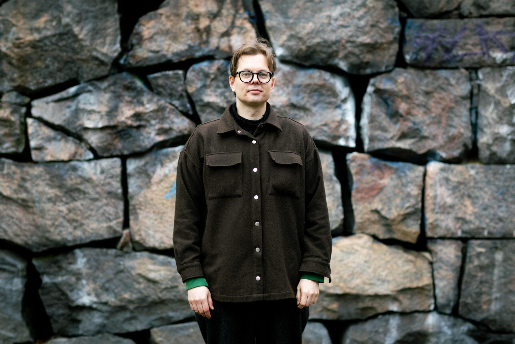 El escritor finlandés Juhani Karila, con gafas y chaqueta marrón, posa contra un fondo de grandes bloques irregulares de granito.