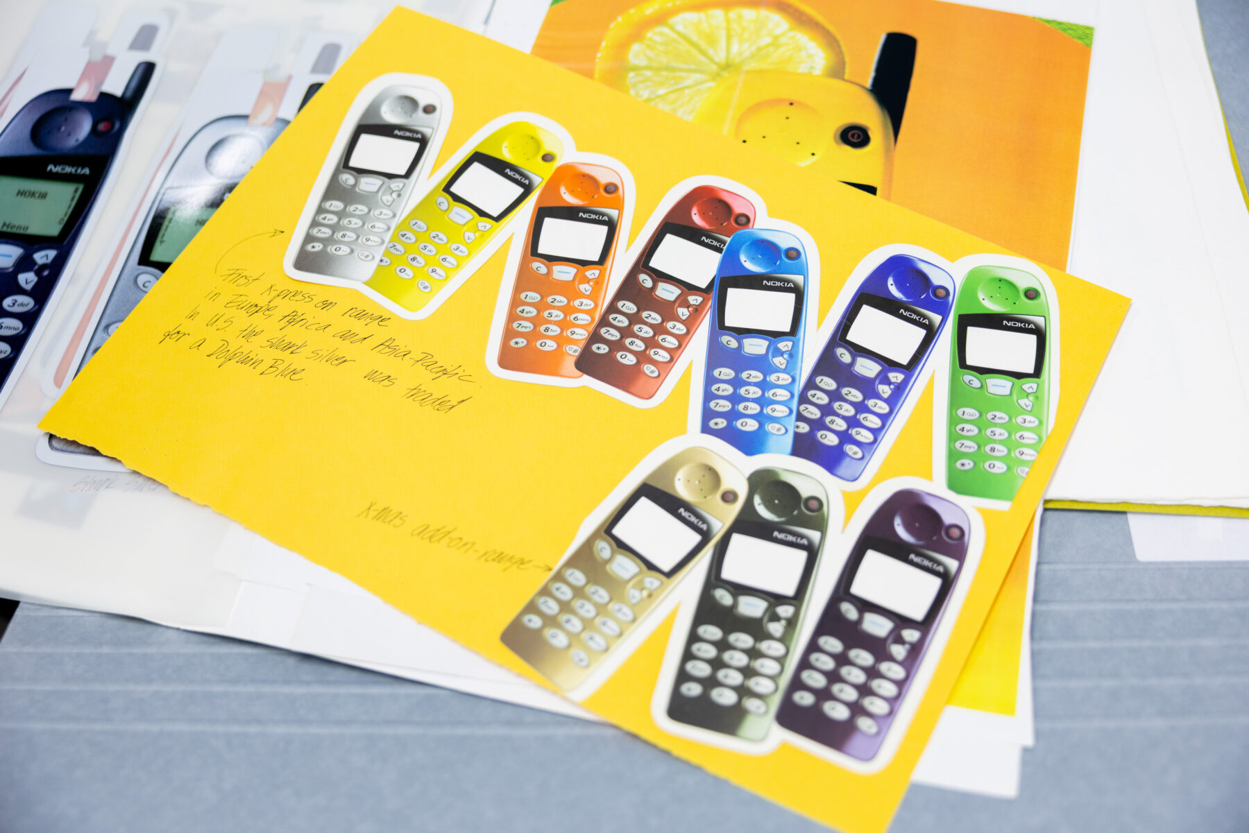 Brightly coloured cutouts of old-style mobile phones are arranged on yellow paper alongside handwritten notes.