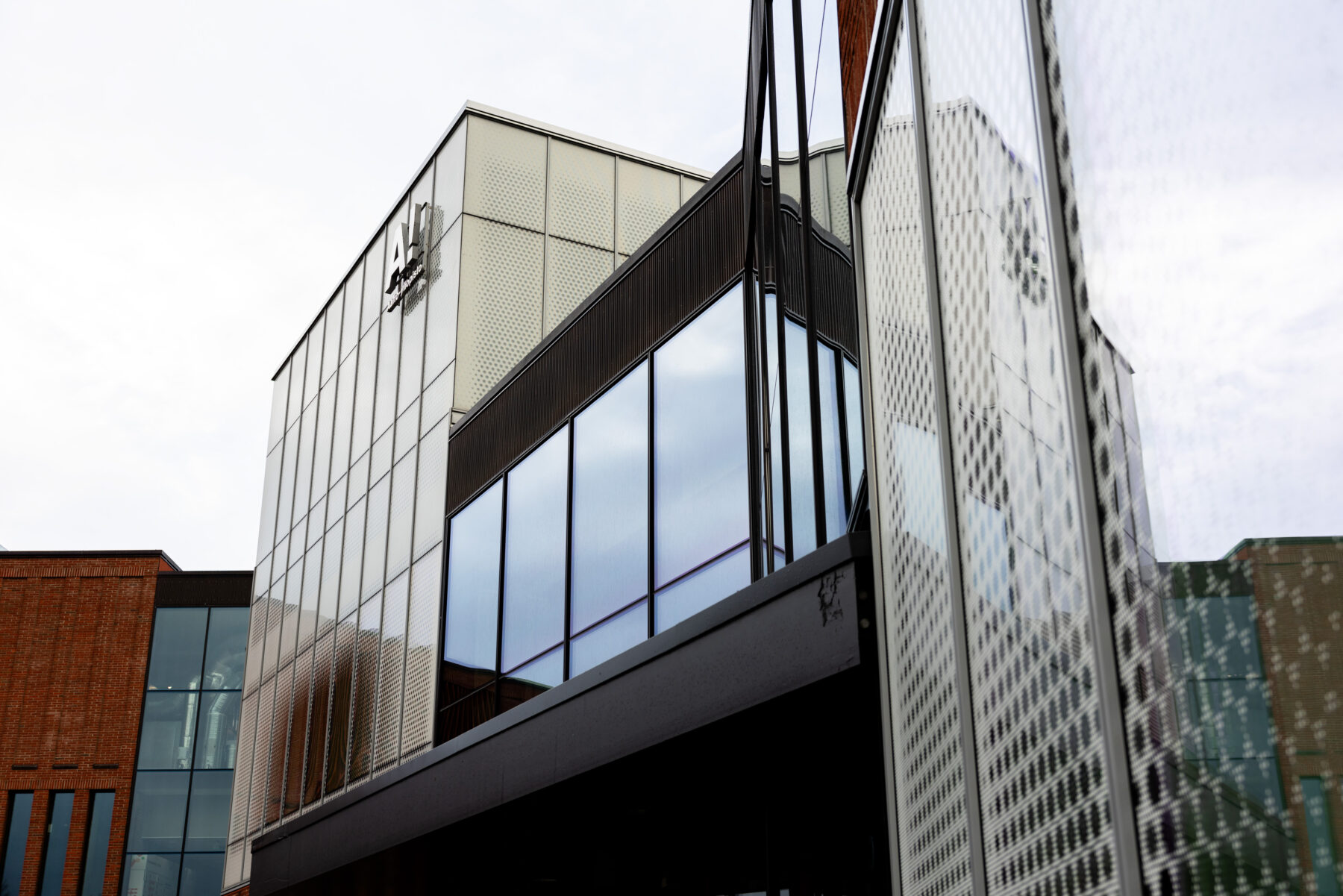 A geometric glass-and-metal facade reflects surrounding architecture under an overcast sky.