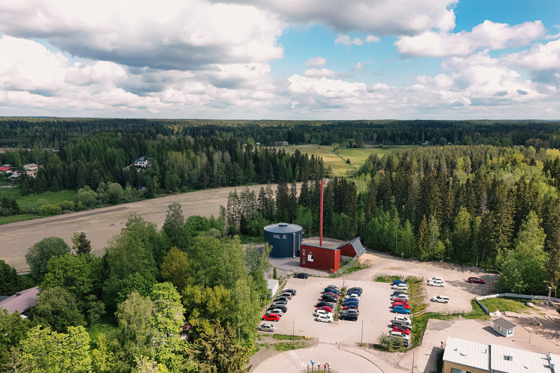 An aerial view shows a silo, a small industrial building and a small parking lot surrounded by trees.