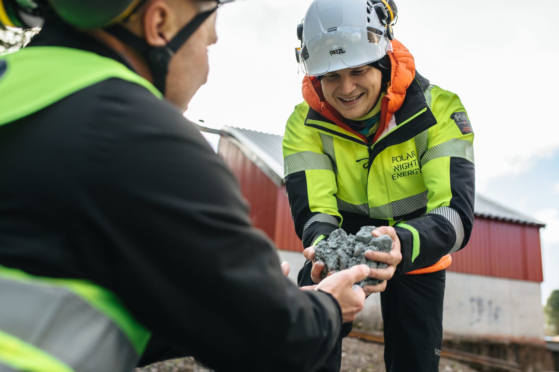 Two people in safety equipment smile as they hold handfuls of crushed soapstone.