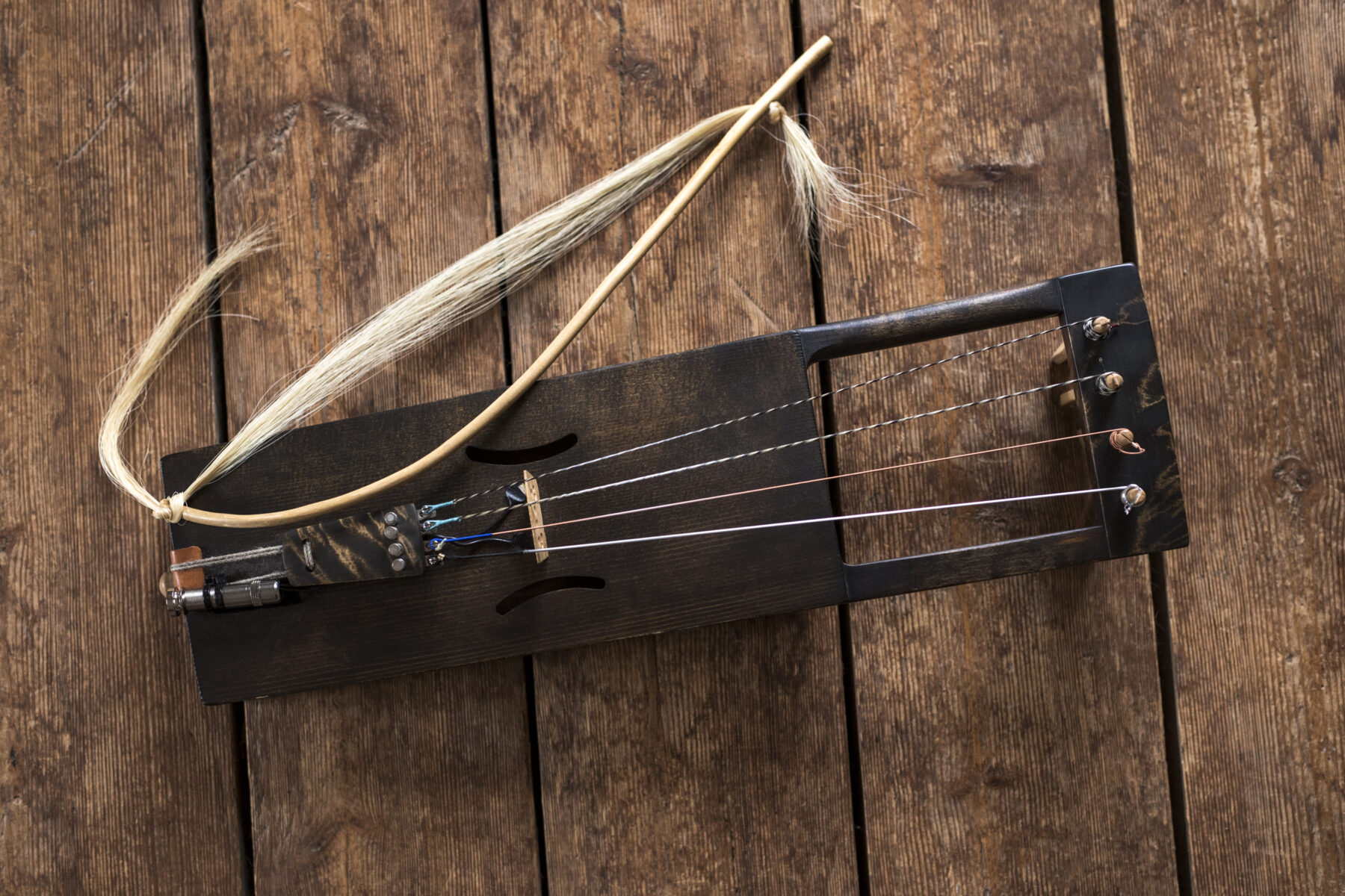A wooden bowed lyre with several strings and a curved bow lies on a wooden surface.