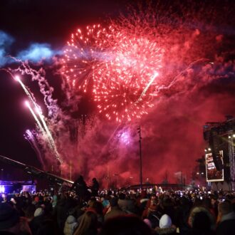 Red fireworks in the sky as a big crowd gathers on a square