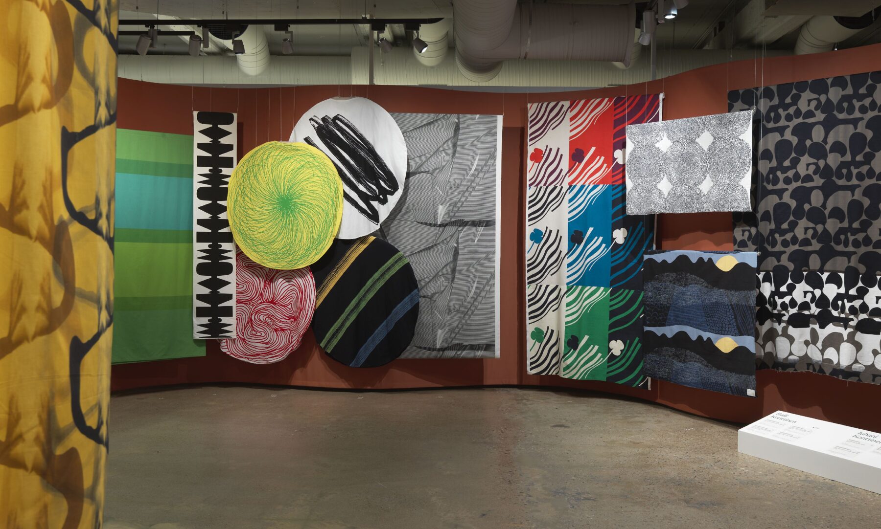 Große Textilien mit auffälligen grafischen Mustern und kontrastierenden Farben hängen im einen Galerieraum des Museums EMMA.