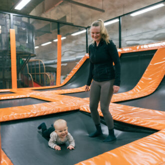 A woman stands on padded trampolines at an indoor play centre in a Finnish civil defencive shelter while her baby crawls nearby.