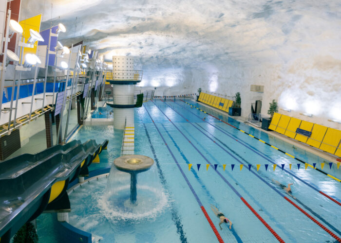 A view of Itäkeskus swimming hall shows lap lanes and water slides built inside a cavernous rock space.
