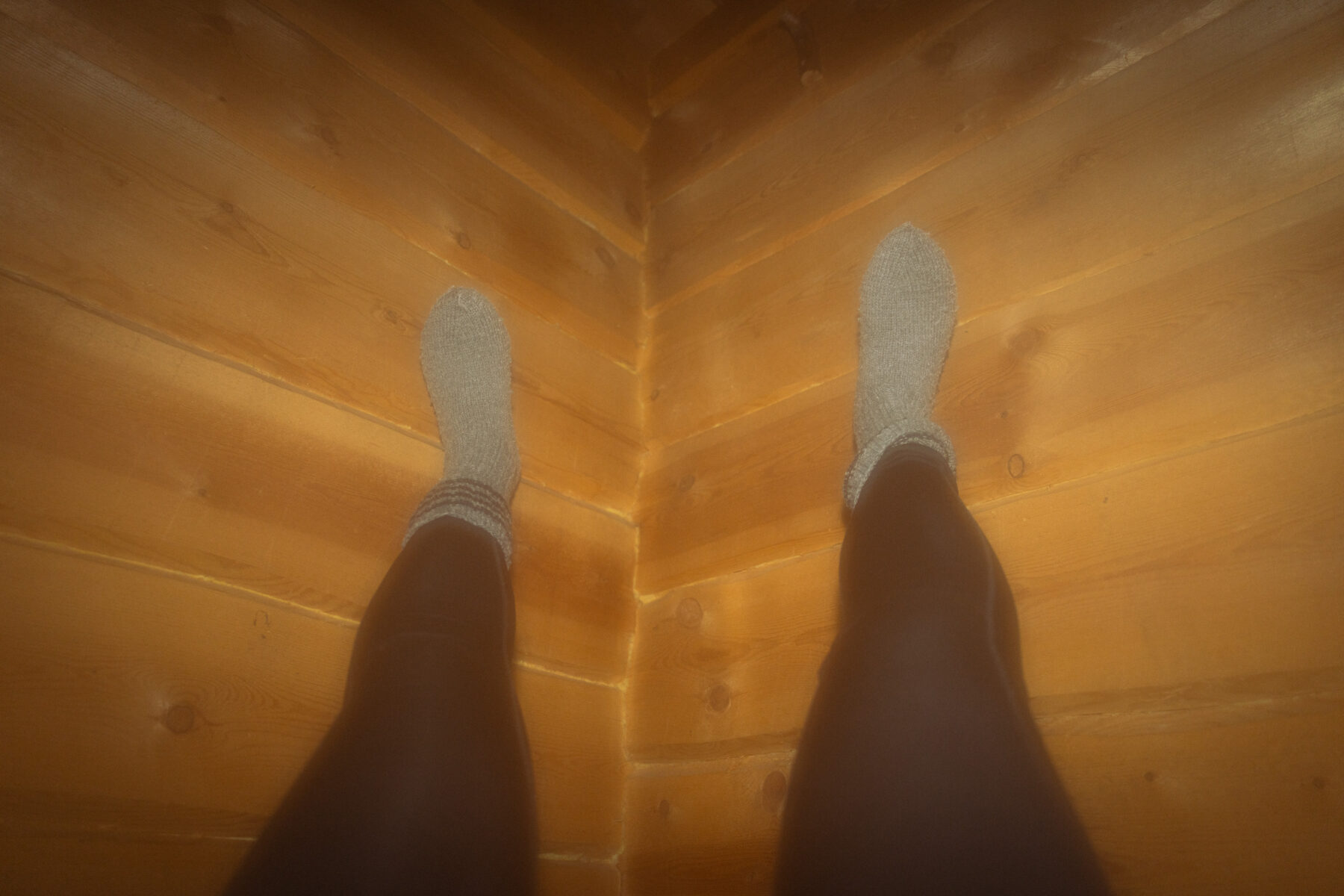 Woolly sock-clad feet are balanced against a warm wooden wall.