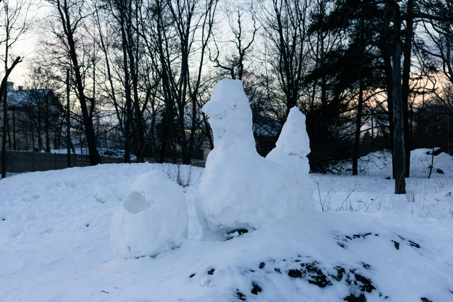 Snow sculptures of a hen and an egg stand in front of trees in a snowy landscape.