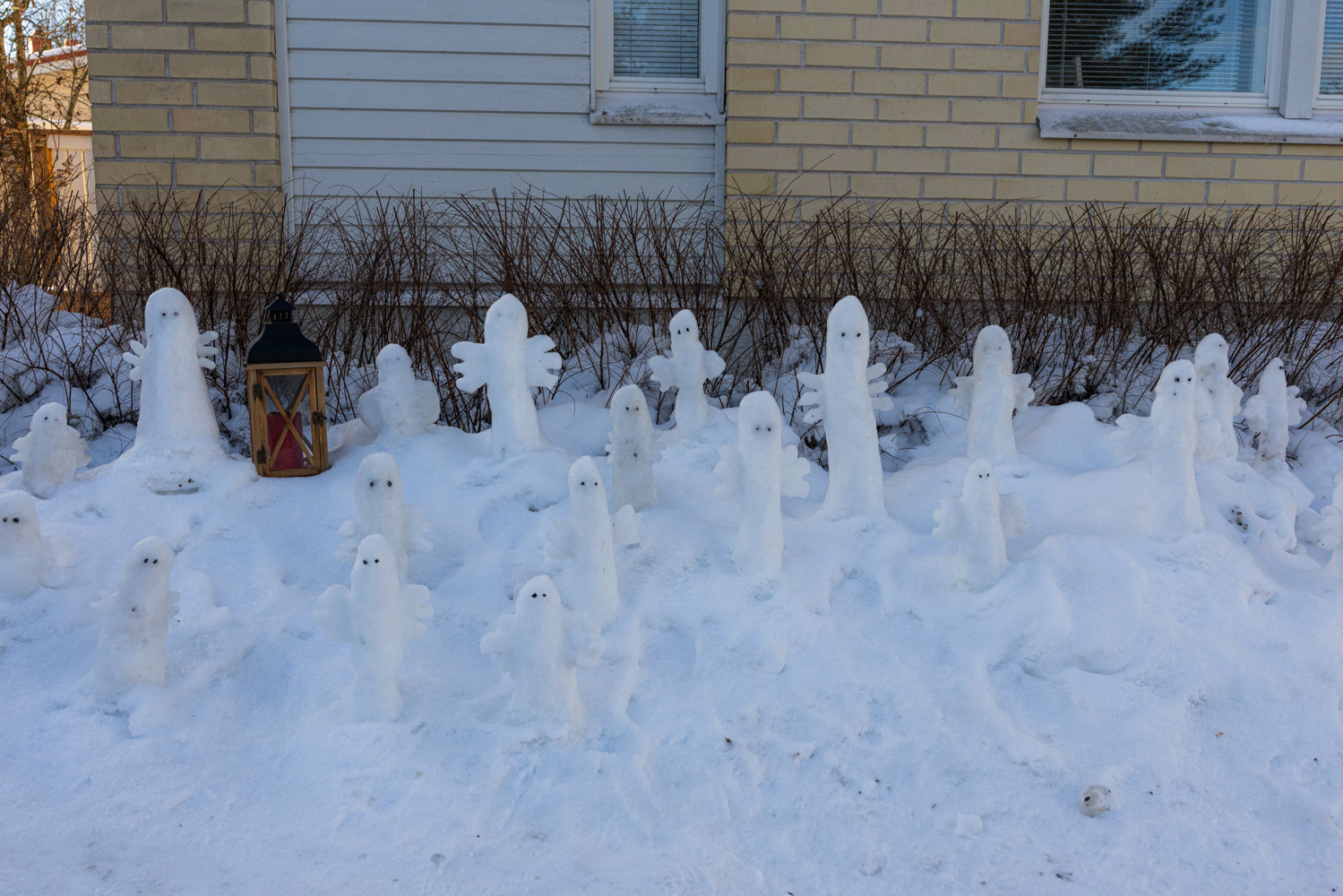 Several dozen small snow sculptures depict Hattifatteners, characters from Tove Jansson’s Moomin books, in front of a brick house.