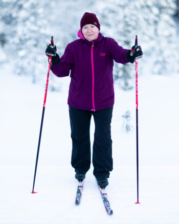 A woman holding ski poles stands on cross-country skis in a snowy landscape.