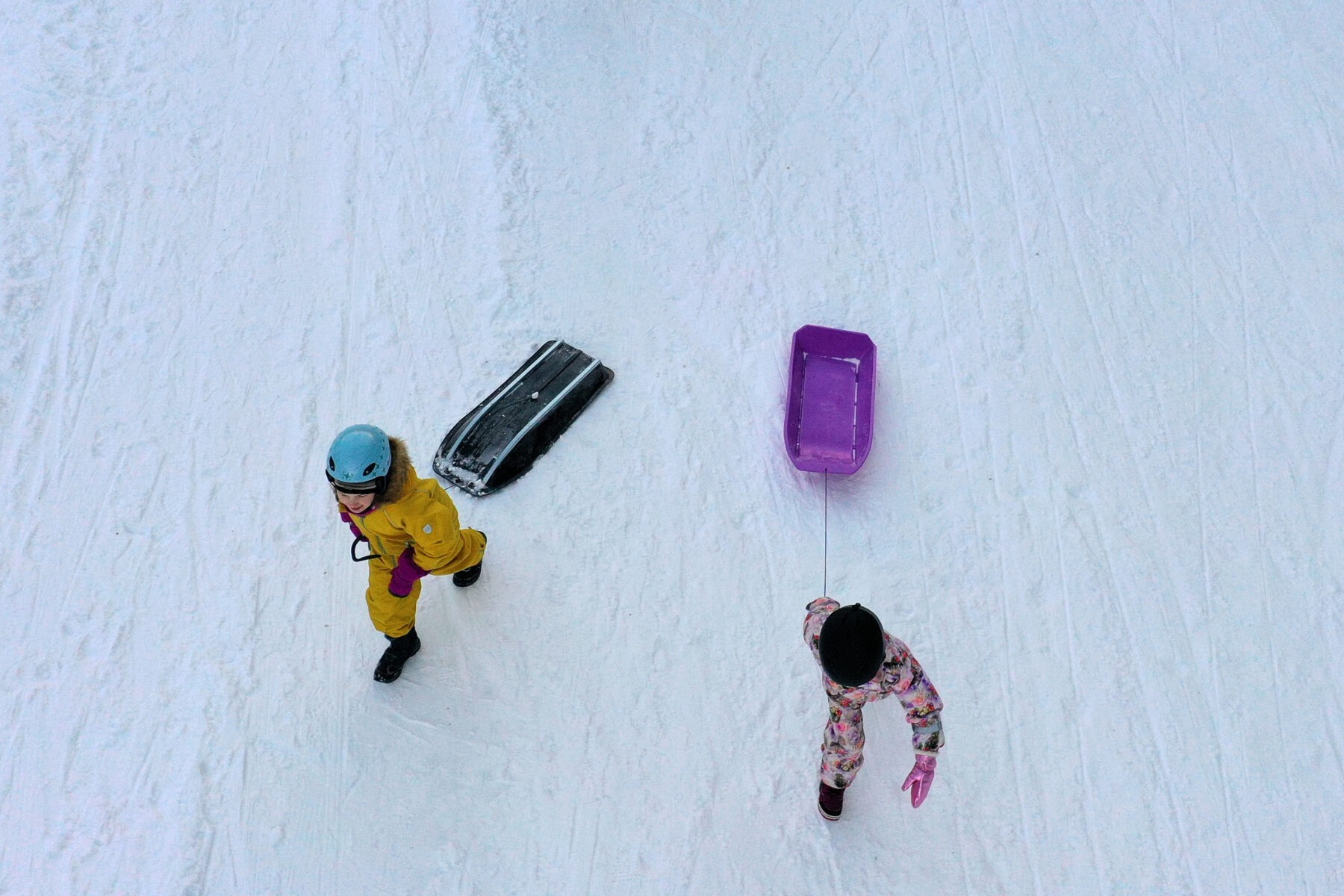 Dos niños van tirando de sus trineos por la nieve.