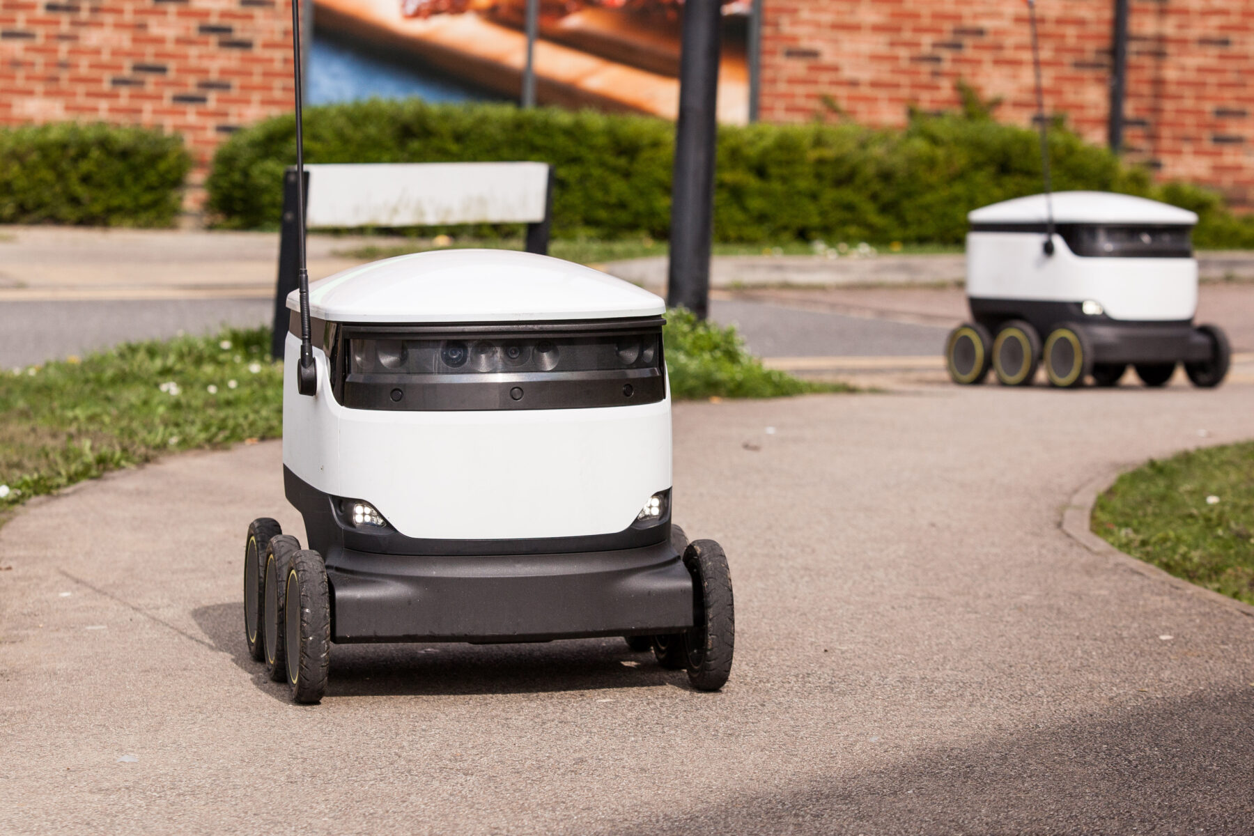 Varios robots repartidores de pequeño tamaño se desplazan por una acera.