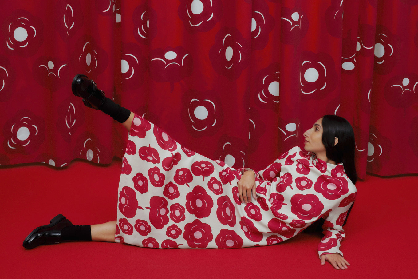 Una modelo ataviada con un vestido estampado de la marca Marimekko posa tumbada de costado en el suelo, levantando una pierna.