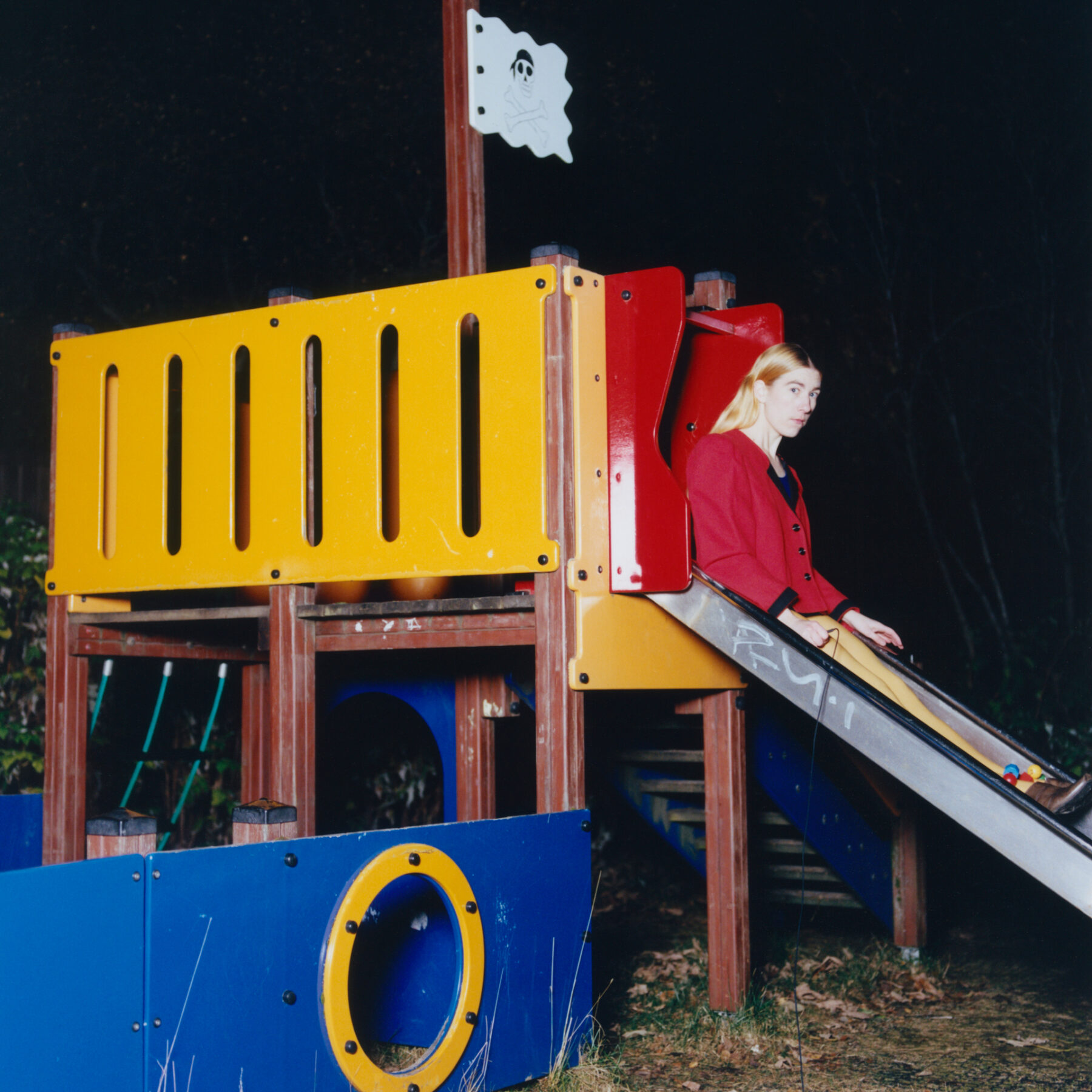 Une femme, en l'occurrence Emma Sarpaniemi, est assise de nuit sur un petit toboggan dans un terrain de jeux pour enfants.