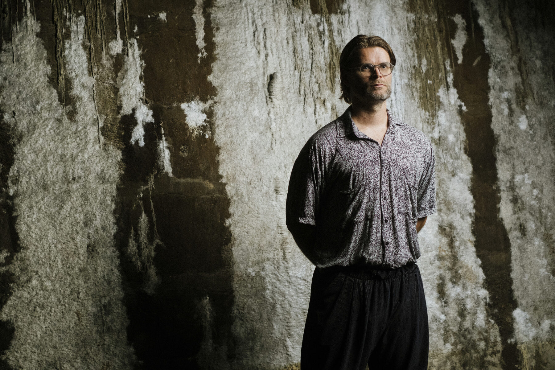 Artist Jakob Kudsk Steensen stands in front of a subterranean rock wall.