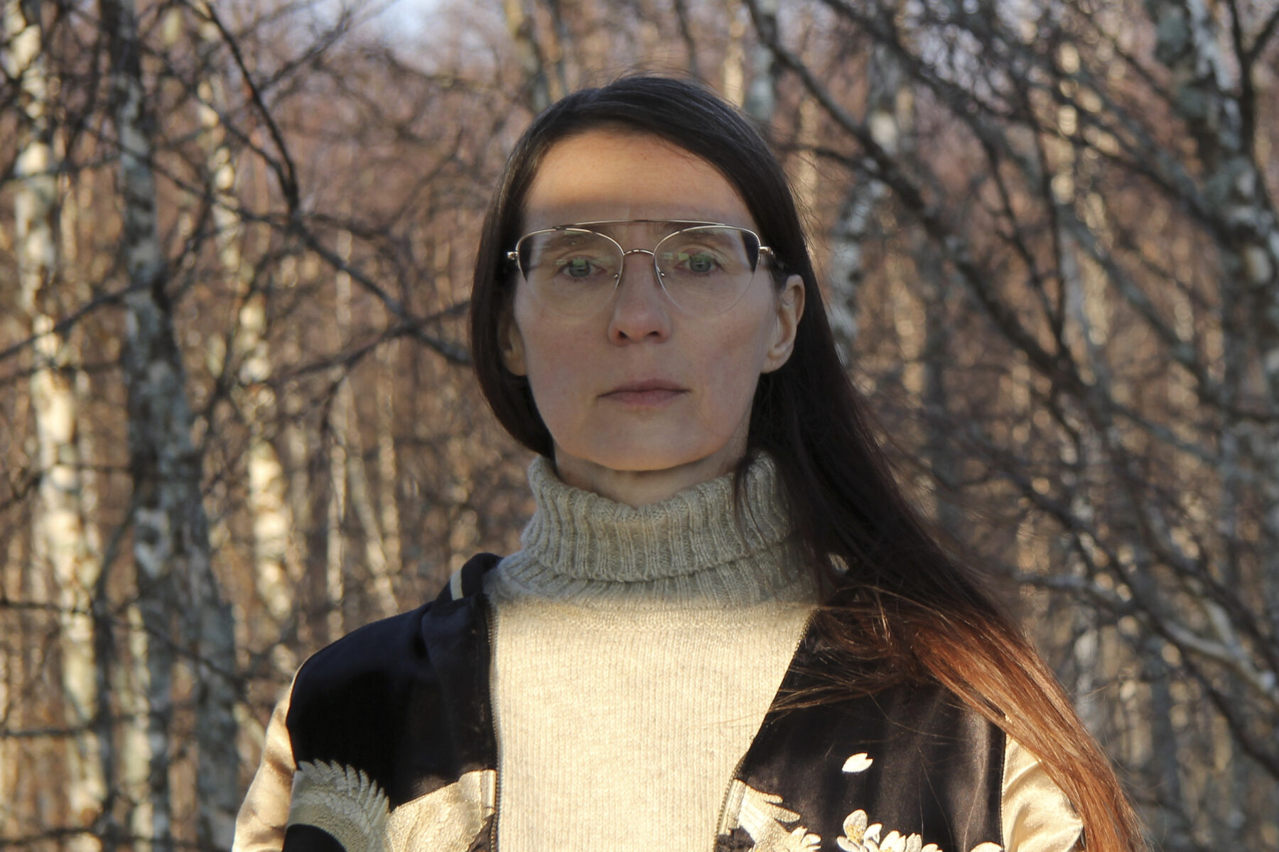 Artist Antye Greie-Ripatti stands in front of bare birch trees.