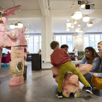 Two women and two kids are in a large indoor space where the children can climb on animal sculptures.