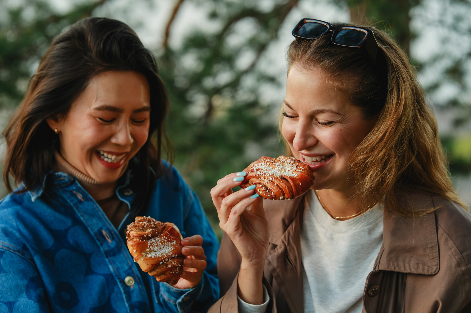 两位女士面带微笑，各自拿着一个芬兰肉桂卷。