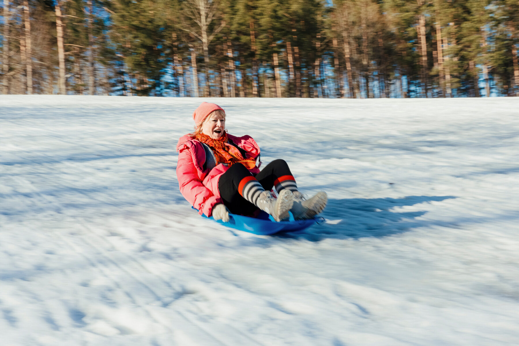 一位女士正乘着蓝色塑料雪橇，从芬兰的雪坡上滑下，脸上洋溢着开心的神情。