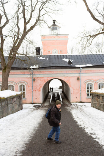 Tim Bird walks along a gravel path towards a pink archway on the island fortress of Suomenlinna, with snow on the ground.