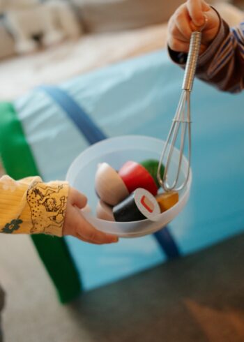 Uma criança segura uma tigela de brinquedos enquanto outra criança mergulha um batedor nela.