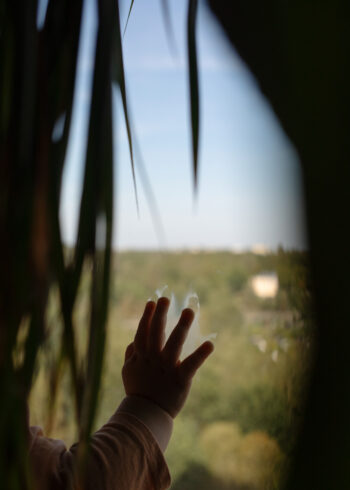 A mãozinha de uma criança pressiona uma janela, com uma paisagem verde brilhante lá fora.