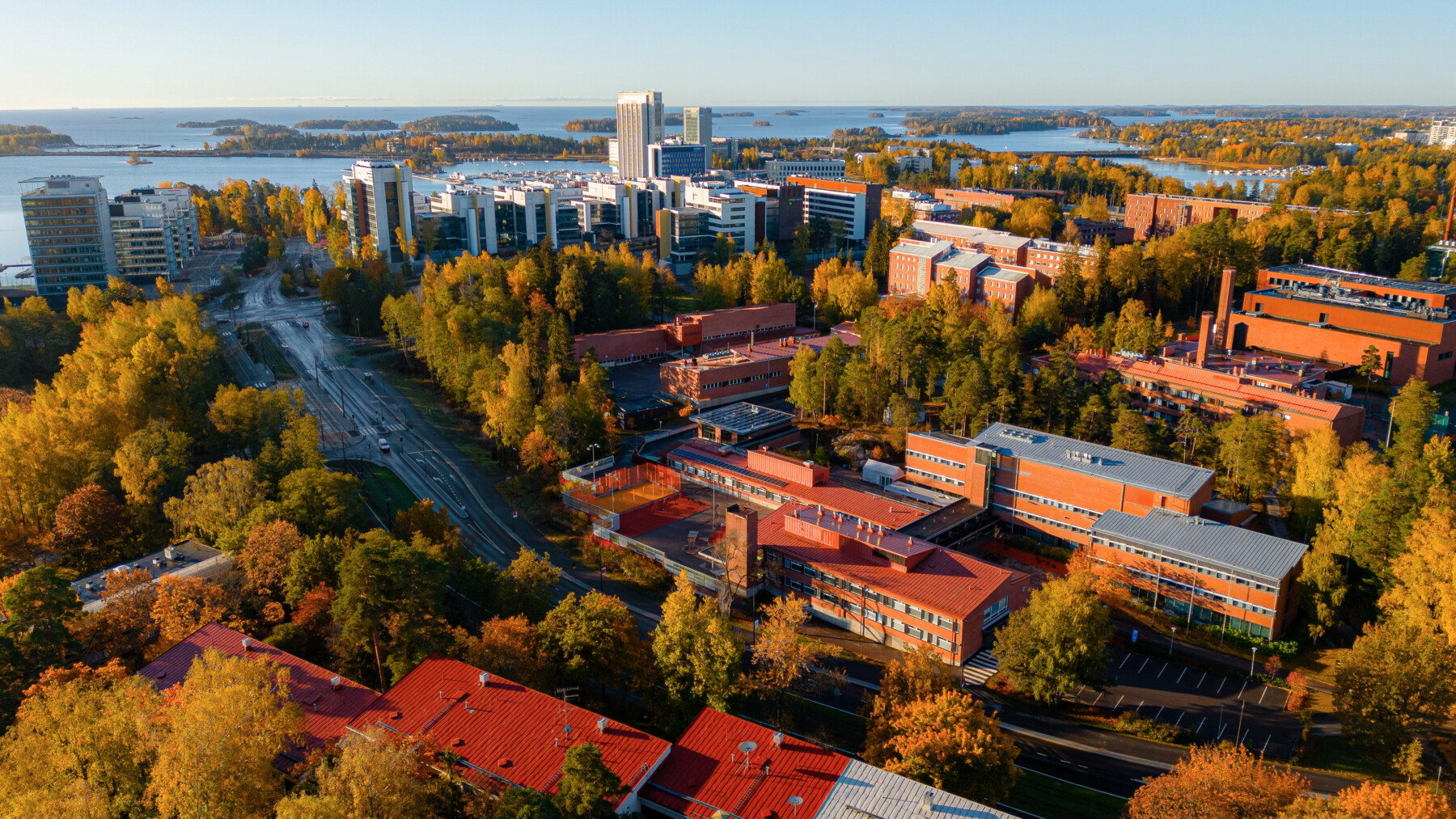 La photo aérienne montre des blocs d'appartements et des bâtiments universitaires entourés d'arbres, devant une baie parsemée d’îles.