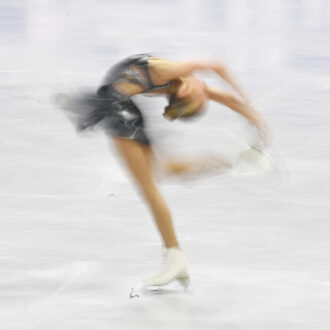 Figure skater Iida Karhunen performs a spin on the ice, arching her back and holding one skate overhead.