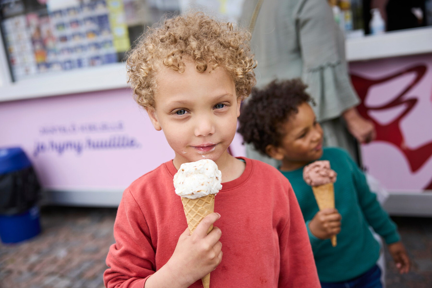 Two children enjoy ice cream beside a kiosk during a warm summer day.