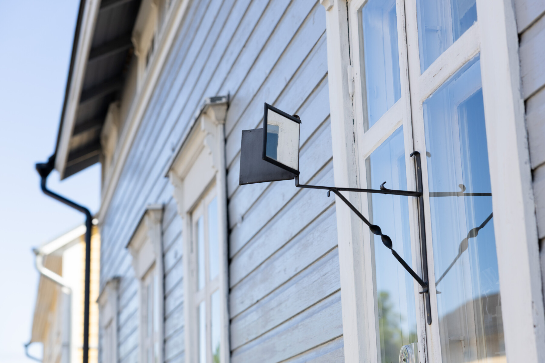 A small metal gossip mirror is mounted outside the window of a pale wooden house in Neristan.