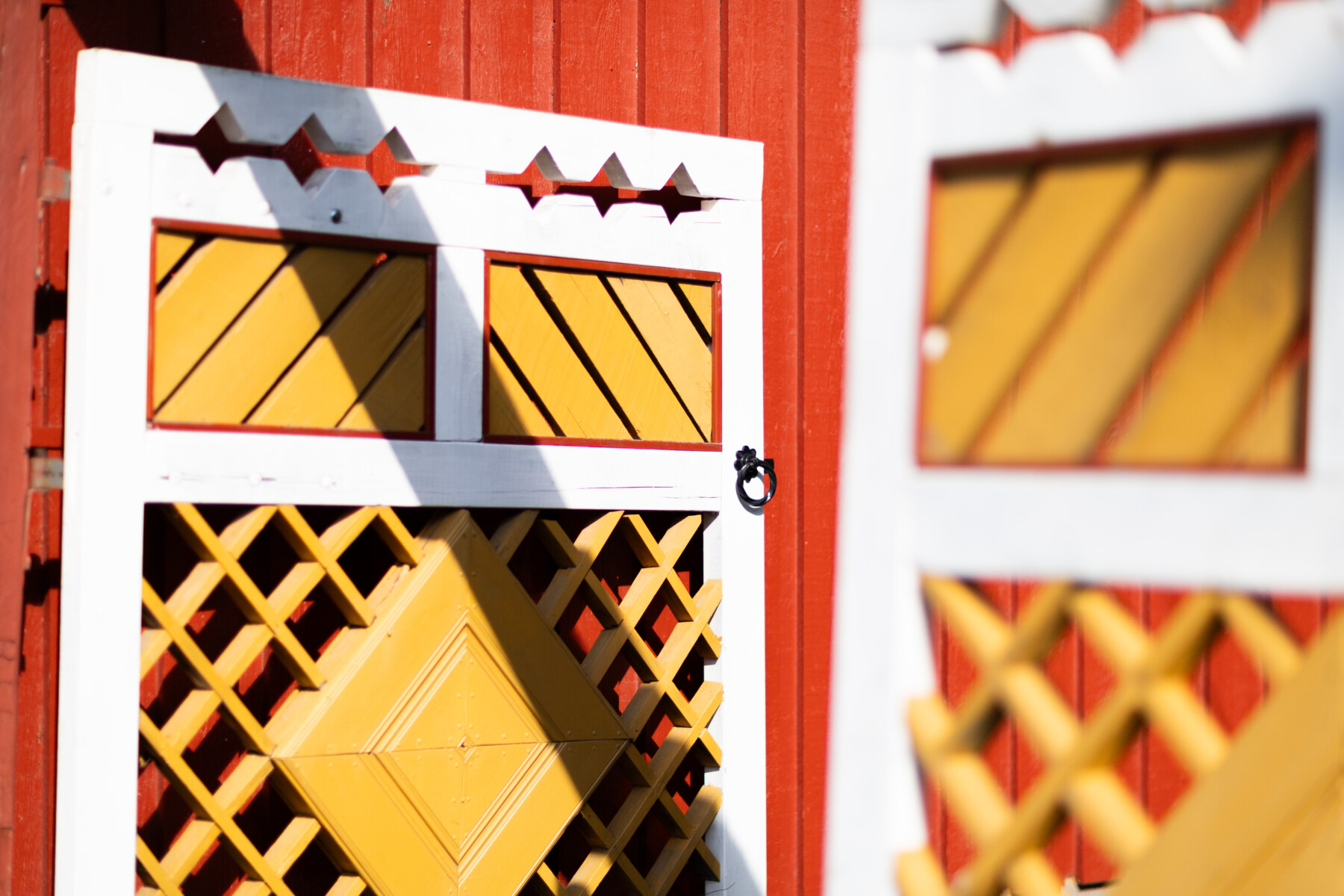 A close view of a brightly painted wooden façade in Neristan shows yellow latticework within white frames.