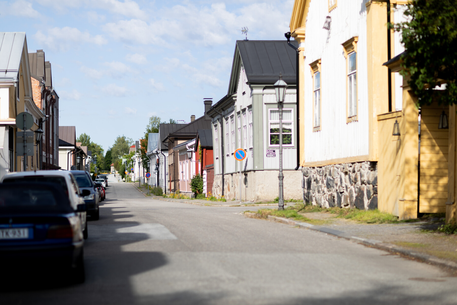 Traditional wooden houses with pastel façades and stone foundations line a sunlit street in Neristan.