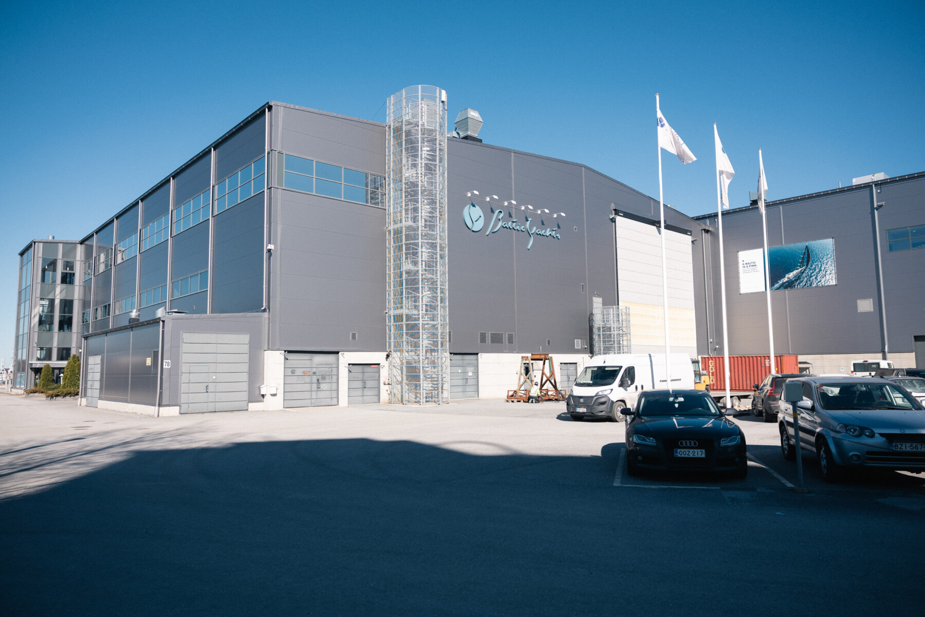 Ein großes Industriegebäude, in dem sich die Produktionsstätte von Baltic Yachts befindet, steht unter einem strahlend blauen Himmel in Pietarsaari.
