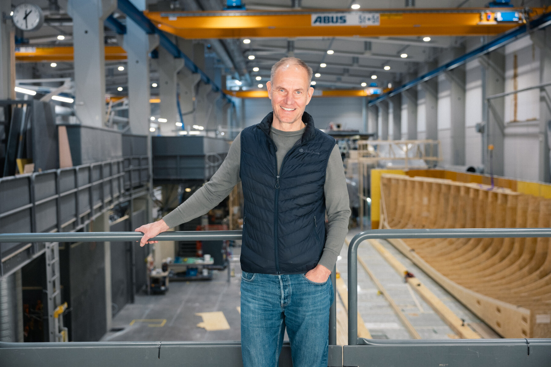 Tom von Bonsdorff, CEO von Baltic Yachts, steht auf einem Laufsteg mit Blick auf eine Werkstatt, in der ein großer Yachtrumpf gebaut wird.