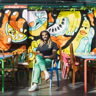 Craft brewer Cleber Gonçalves sits among brightly coloured tables and chairs in front of a vibrant mural at CoolHead Brew.