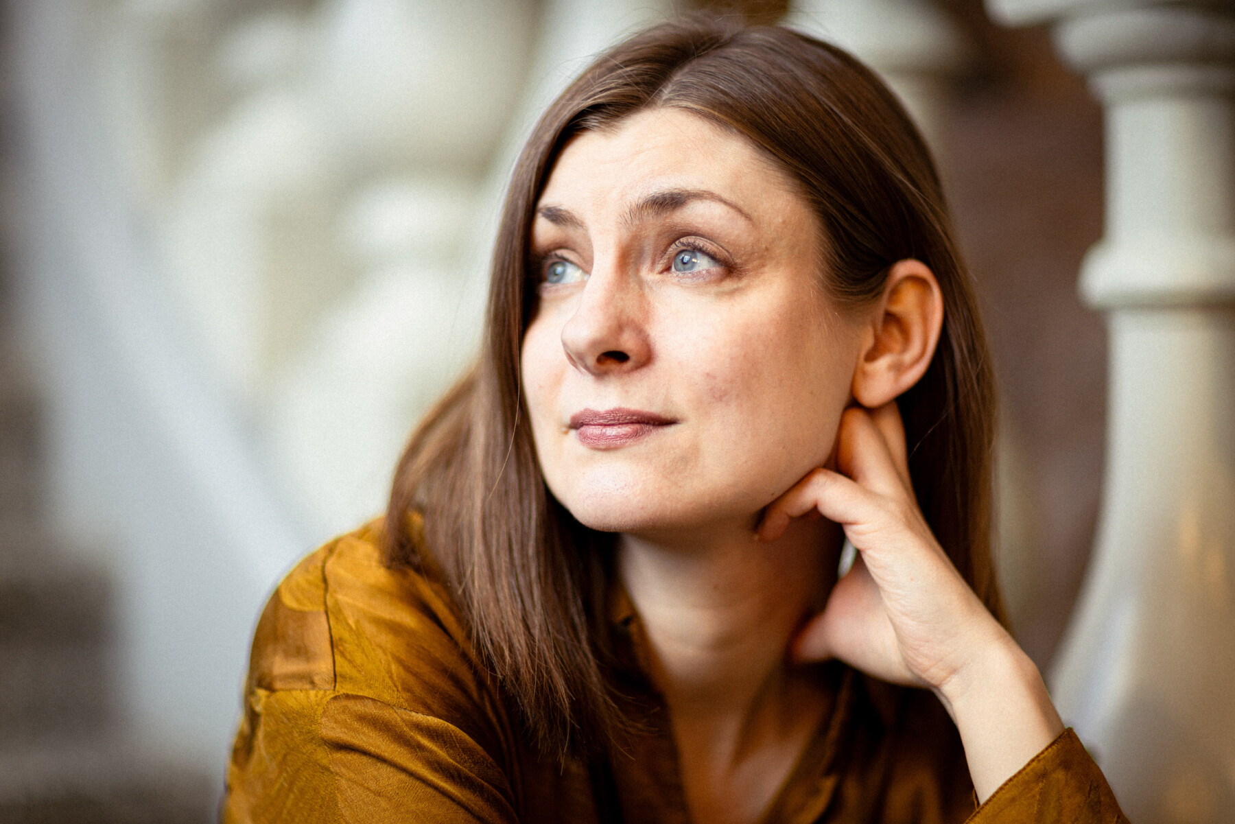 Author Iida Turpeinen sits on a staircase at the Finnish Museum of Natural History, resting her head on one hand with white balustrades blurred in the background.