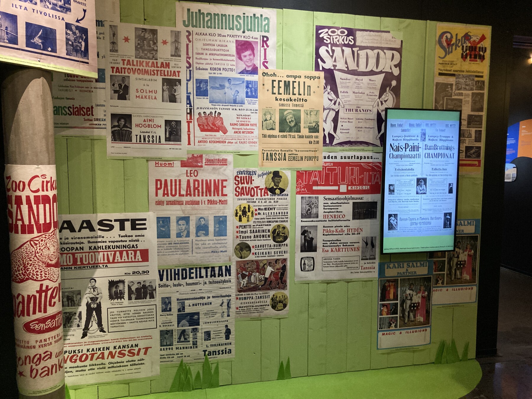 Historic Finnish circus posters and advertisements from different eras are displayed side by side on a green wall in the Theatre Museum.