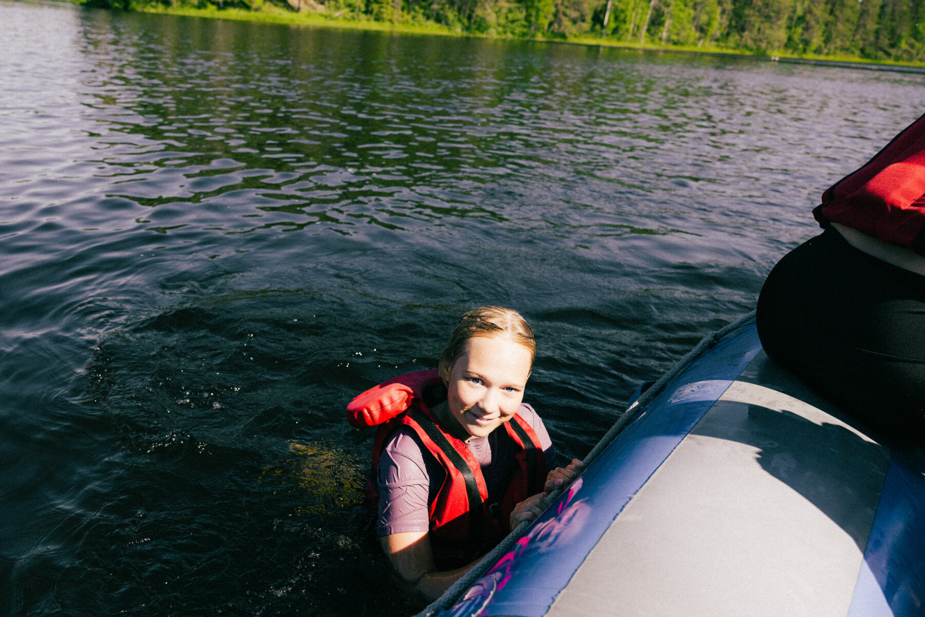 A child in the water grips the edge of an inflatable raft during a summer rafting trip in Finland.