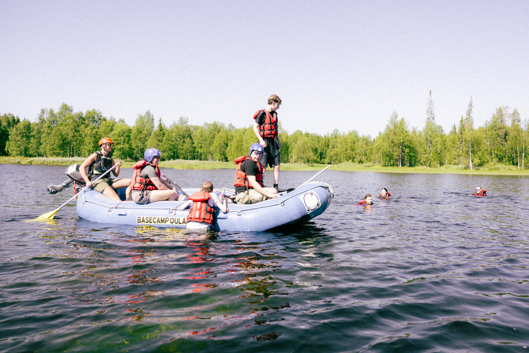 Rafters in red life jackets pause on the water beside swimmers during a summer rafting trip on the Kitka River.
