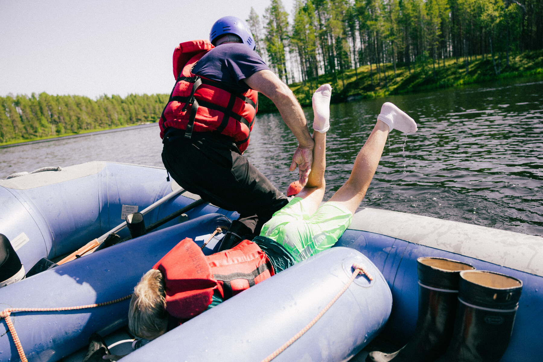 An adult helps a young rafter back into the boat while floating on a forest-lined river.