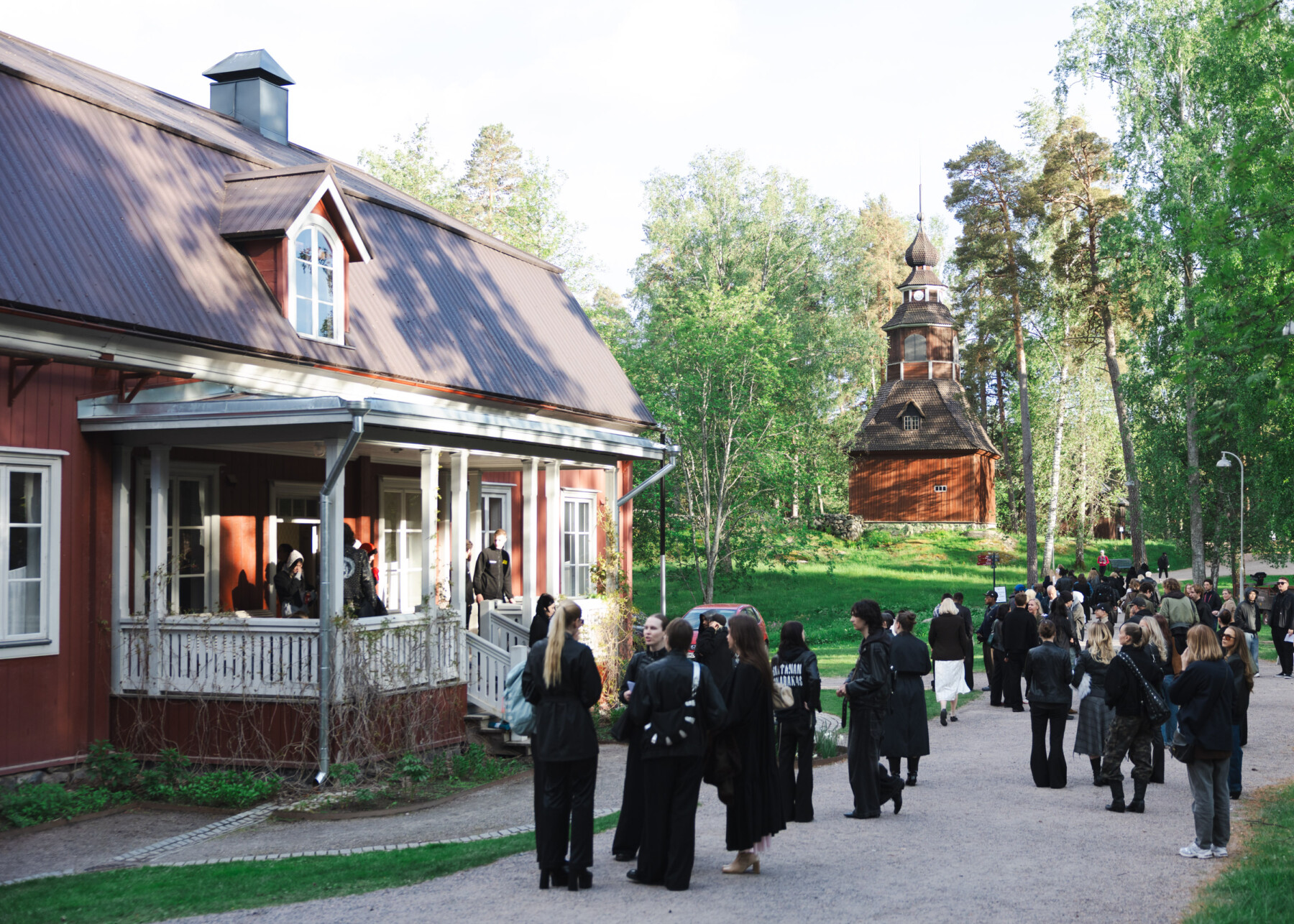 Visitors gather outside a historic red wooden building on the island of Seurasaari during a Helsinki Fashion Week event.