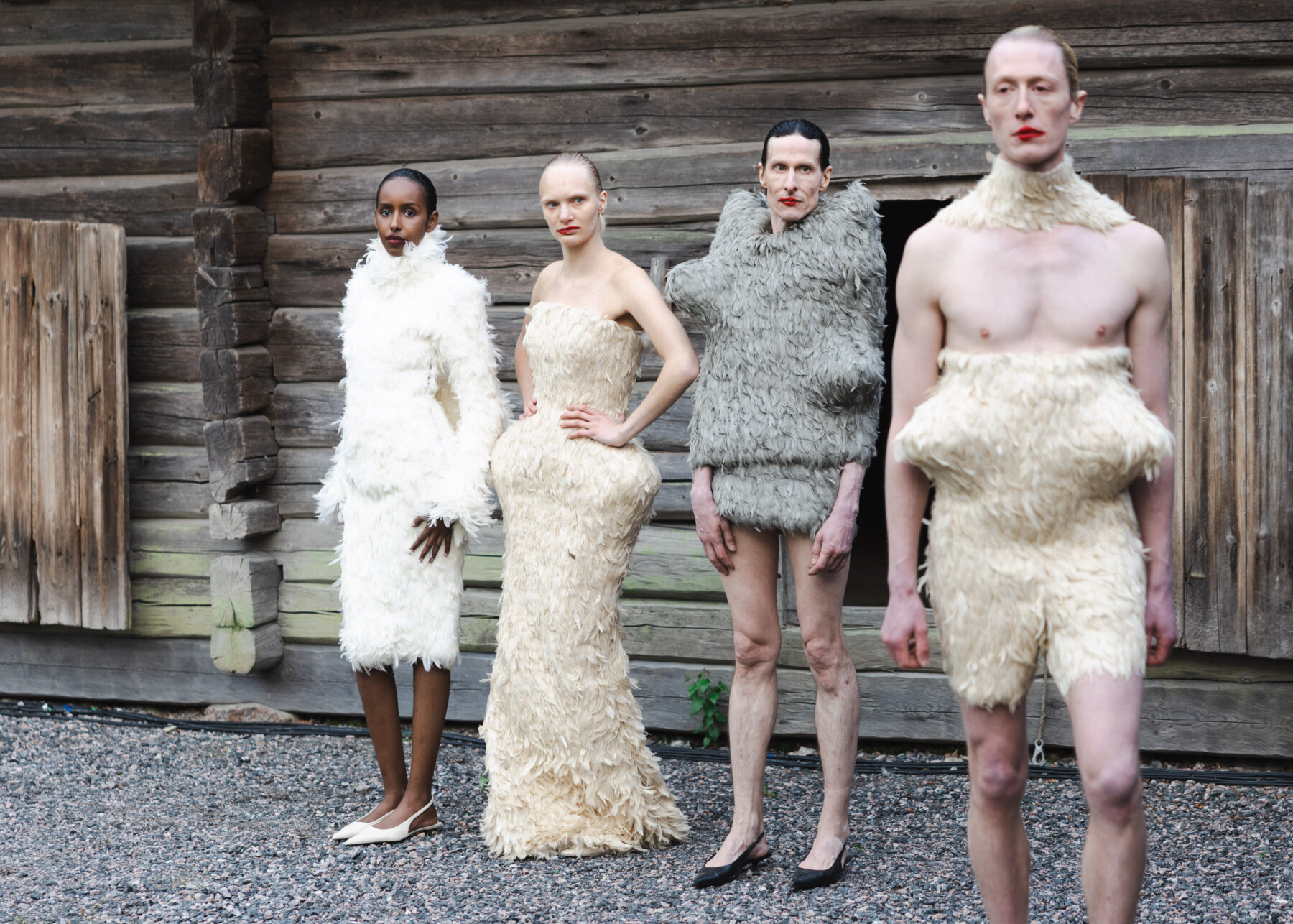Models pose in textured cream and grey outfits designed by Ilari Kokkola with unconventional shapes and fuzzy surfaces against the backdrop of a traditional timber structure.