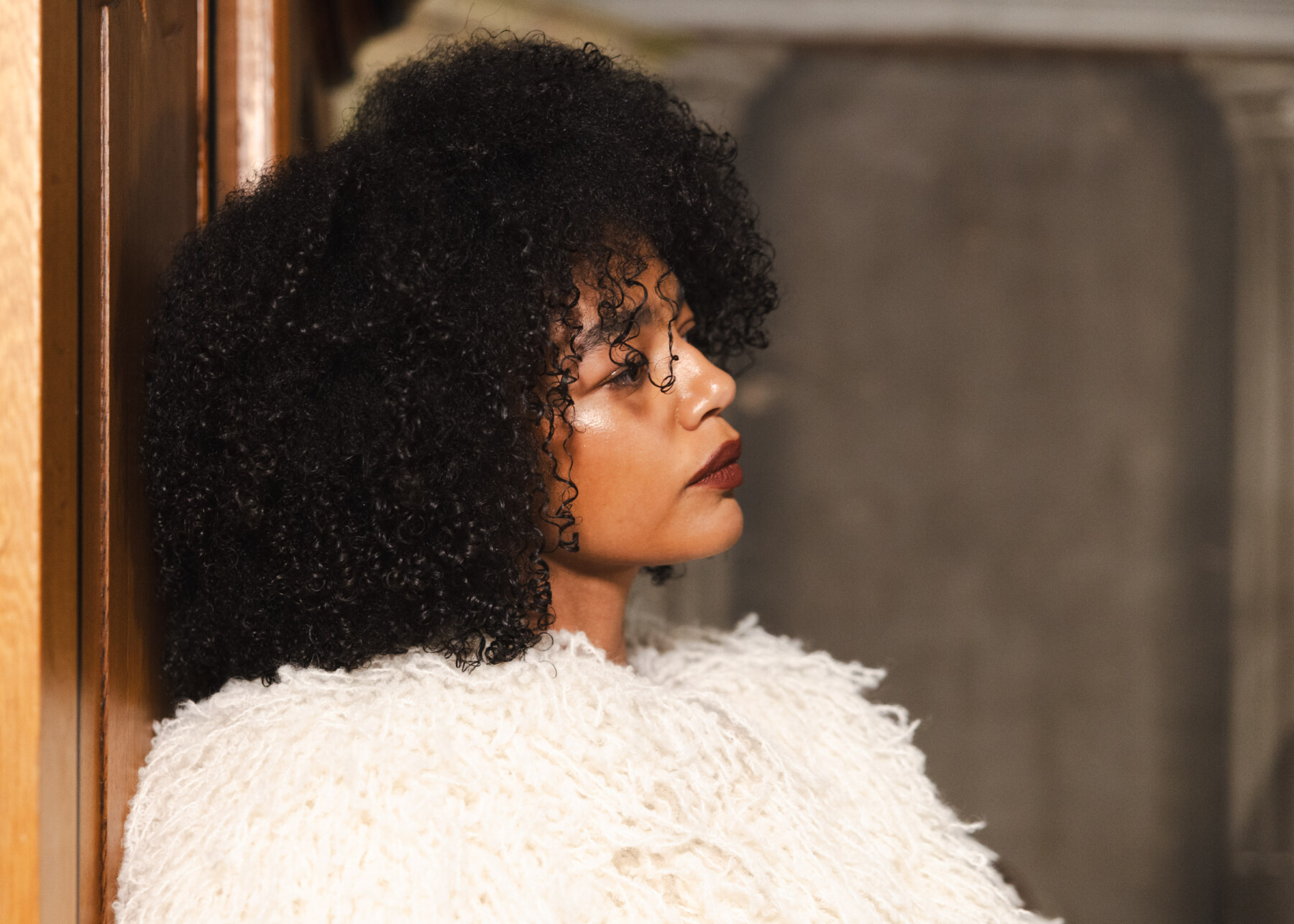 A model wearing a textured white garment by Idaliina Friman leans against a wooden doorway.