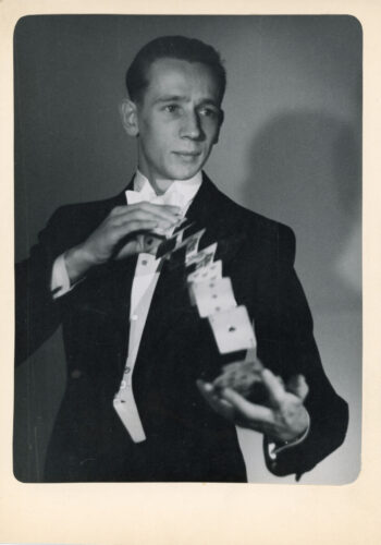 Magician Solmu Mäkelä performs a card flourish in formal evening dress, with a cascade of playing cards suspended between his hands.