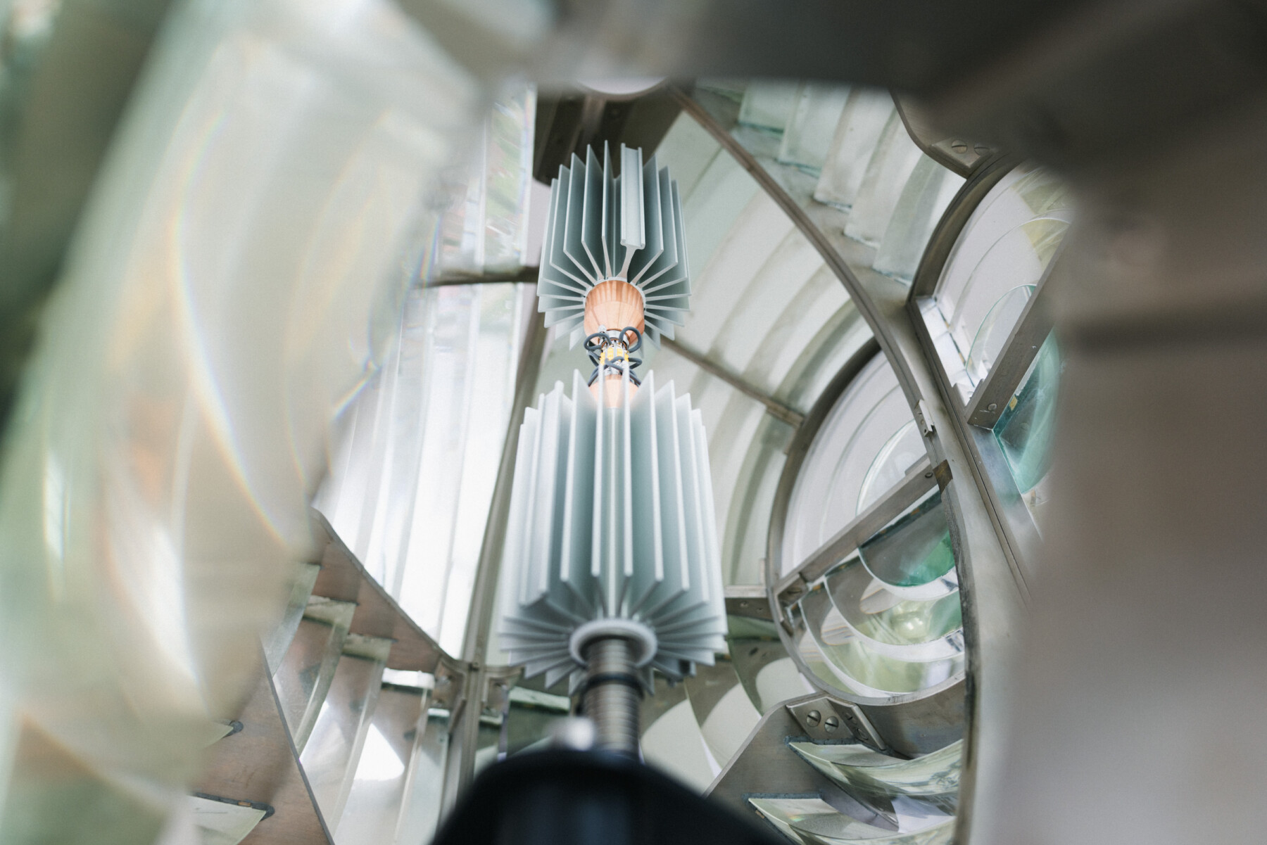 The lighthouse lamp and surrounding Fresnel lens components inside Marjaniemi Lighthouse in Hailuoto are seen from below through the structure's glass and metal framework.