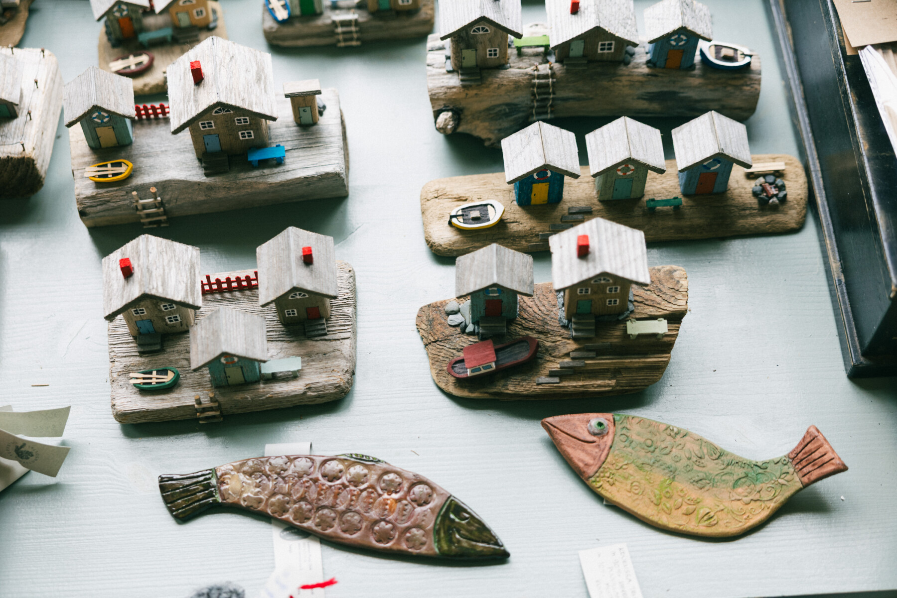 Handmade craft models of small seaside cottages on driftwood bases are displayed in a shop on Hailuoto, alongside decorative fish-shaped ornaments.