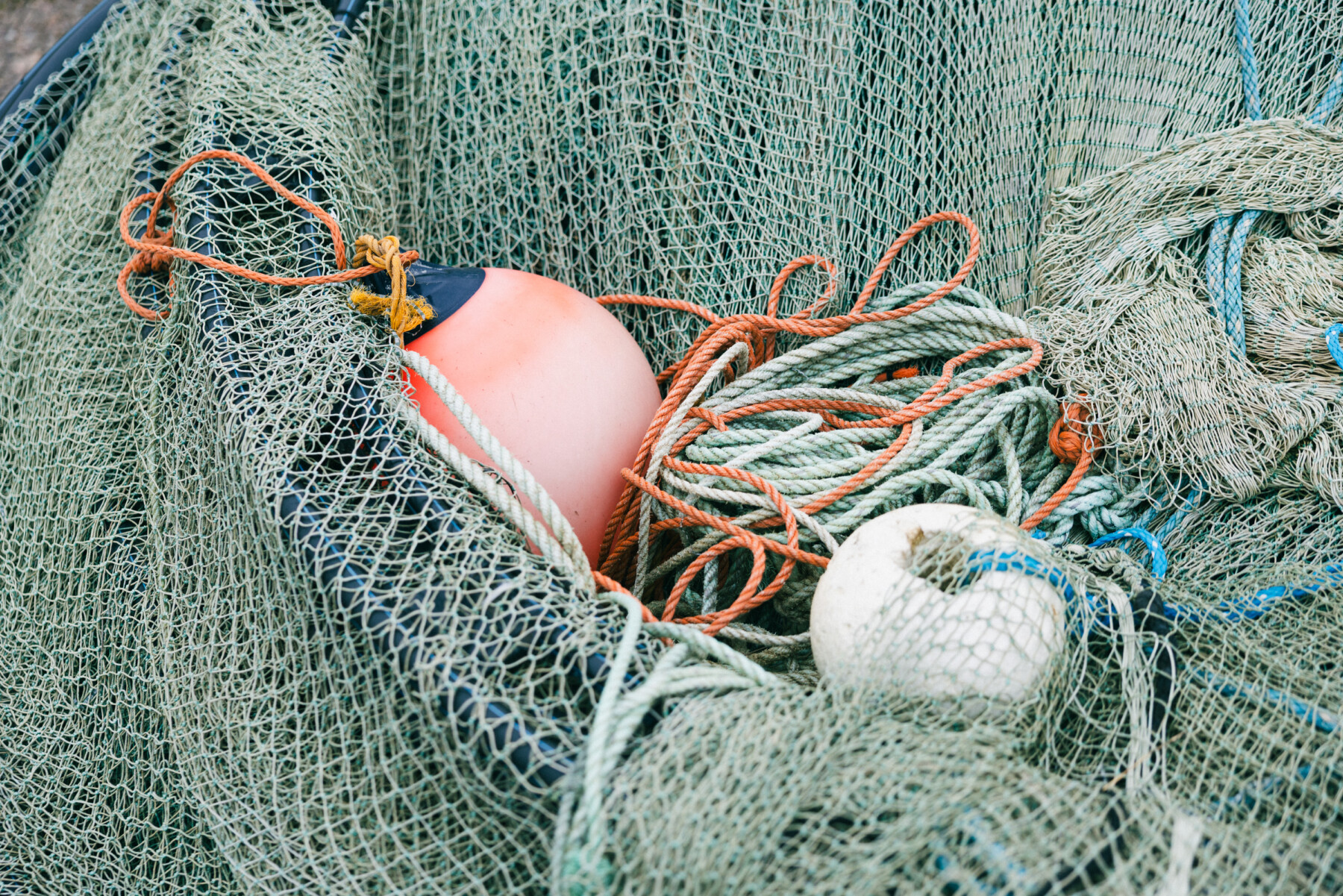 A pink float, white buoy and coiled ropes lie among large fishing nets in a close up view.