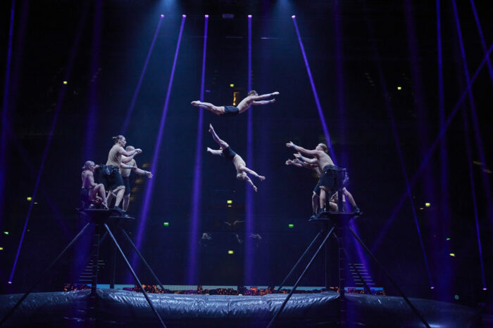 Acrobats launch and catch one another between raised platforms above a safety mat during a performance by Arctic Ensemble.