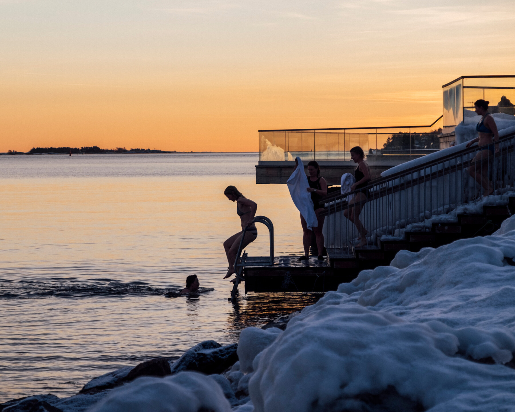 People enter the water from a pier in a winter landscape.